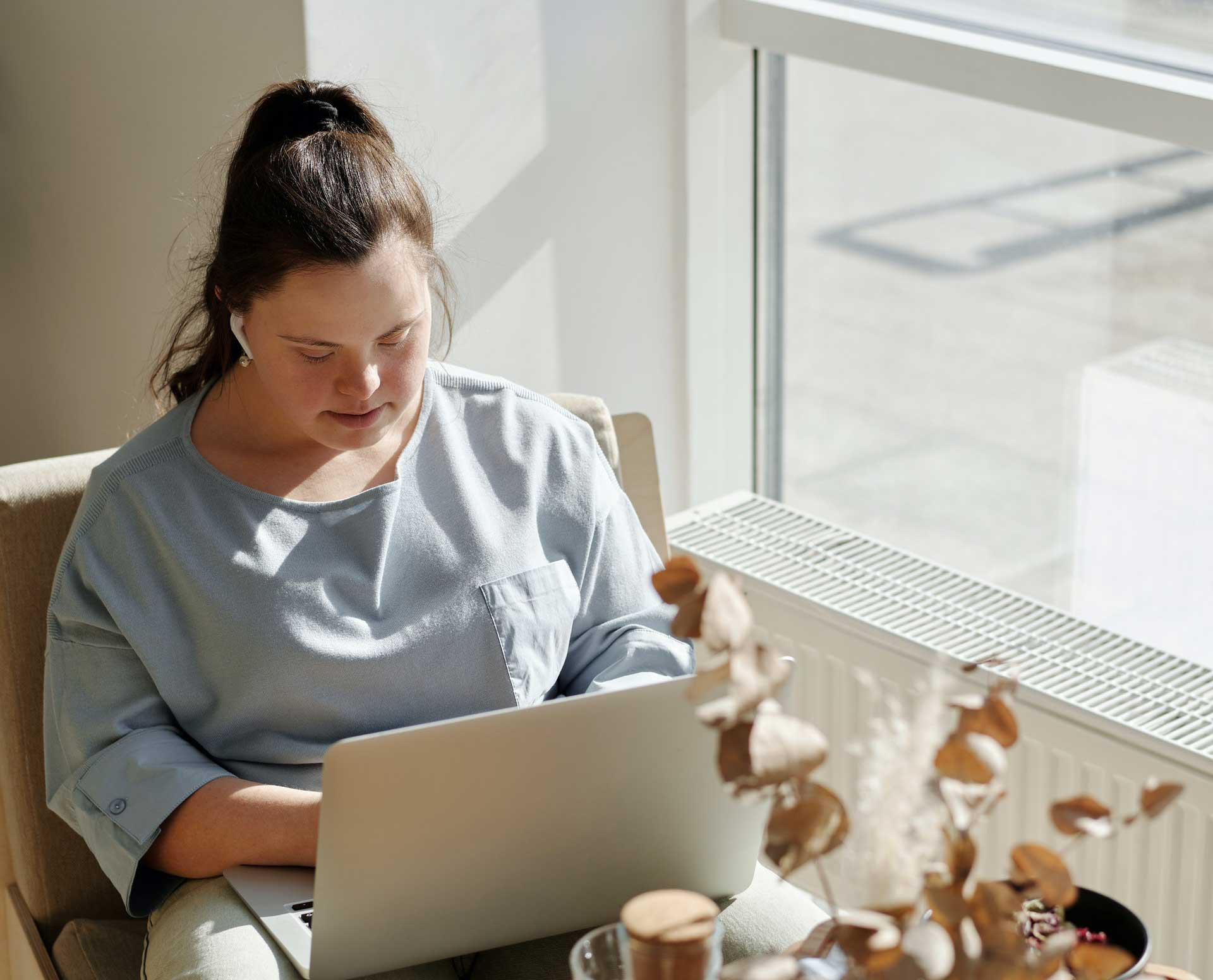 Woman on laptop with earbuds in light filled space