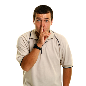 A First Nations man with his finger on his lips in a 'shh' gesture. 