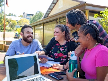 A group of people sitting outside having a conversation near a laptop. 