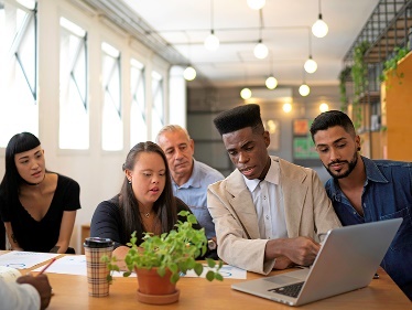 A group of people in a meeting looking at a laptop together. 