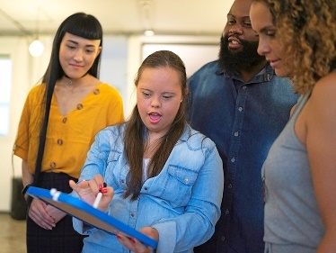 A person with disability showing a group of people something on a clipboard. 