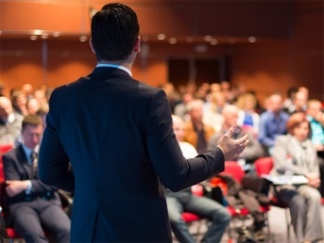 A person in a suit talking to a crowd of people.