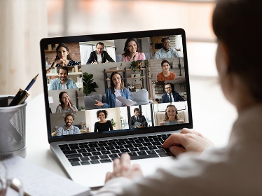 A person on a laptop in a video call with many people.