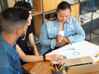 A group of people working on a document together with a lapotp open in front of them. 