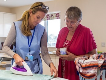 A support person is helping someone iron clothing. 